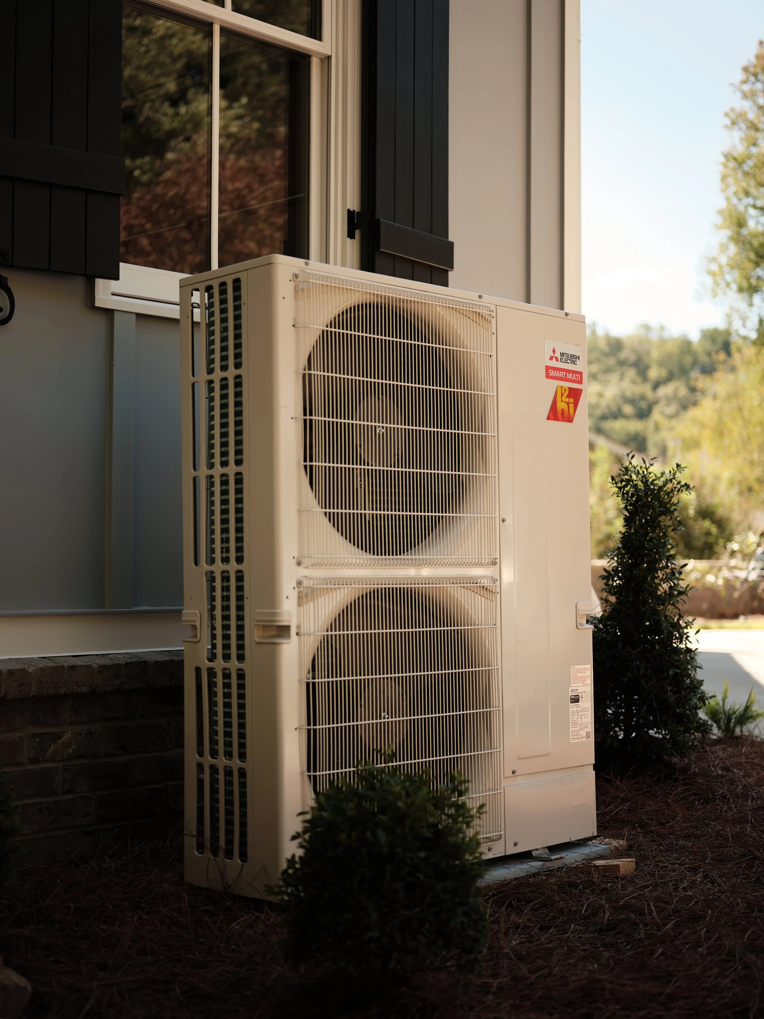 Mitsubishi heat pump outdoor unit installed beside a home in summer